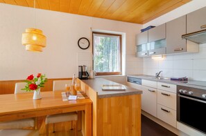 Uma cozinha moderna com armários de madeira, forno embutido e uma área de refeições com mesa e cadeiras de madeira.