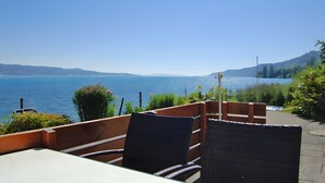 A terrace with wicker chairs and a table overlooking a lake.