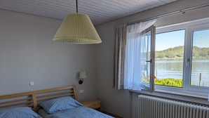 A bedroom with two beds, a window with a view of a lake, a lamp, and a radiator.