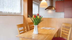 Ein Holzespeisezimmer mit einer weißen Blumenvase, Holzstühlen und einer Küchenzeile mit Schränken und einer Pendelleuchte.