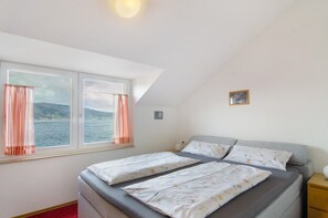 Une chambre avec deux lits, une fenêtre avec des rideaux, une table de chevet et un tableau accroché au mur.