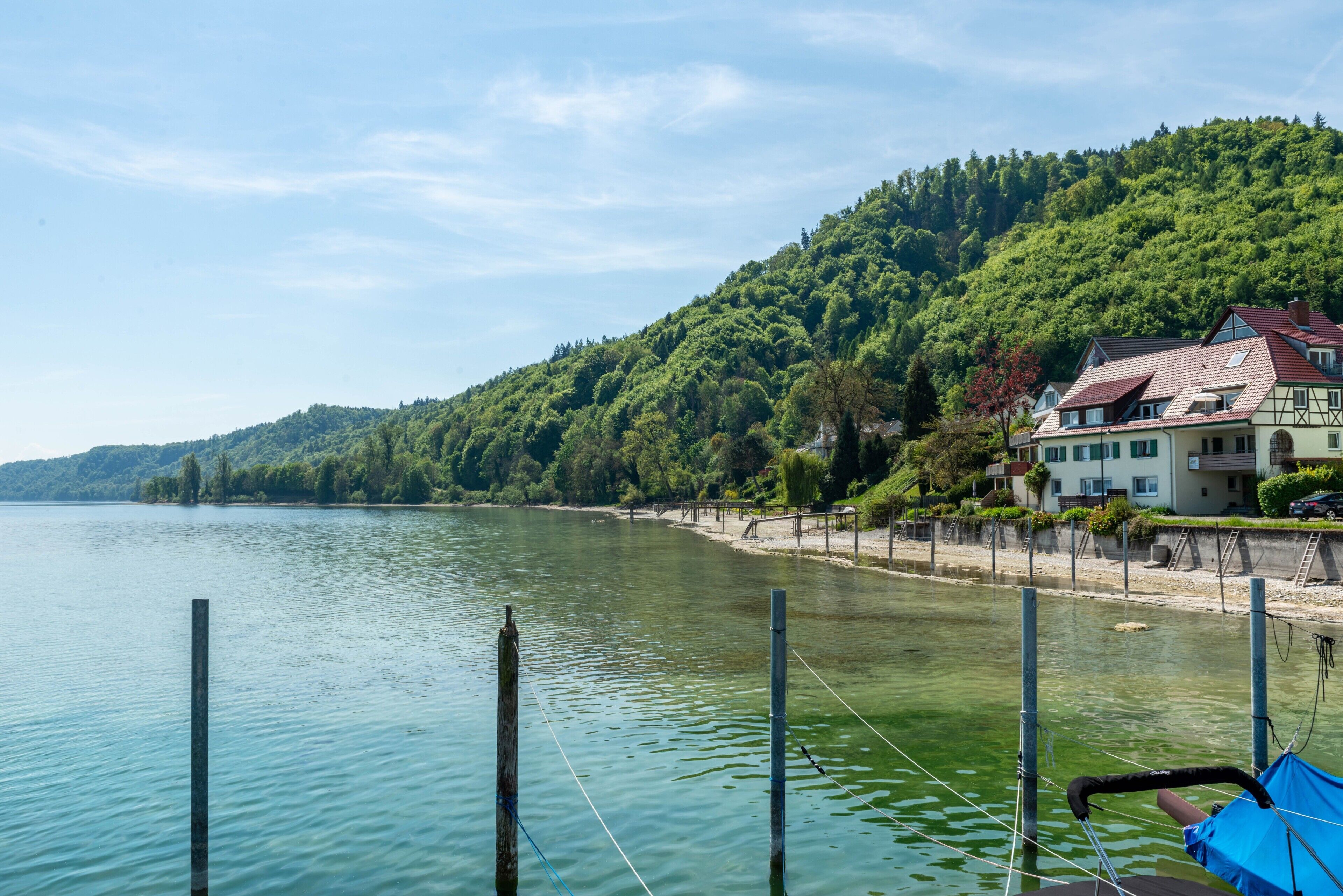 A lakeside view with a house on a hillside, a dock with a boat, and calm water.