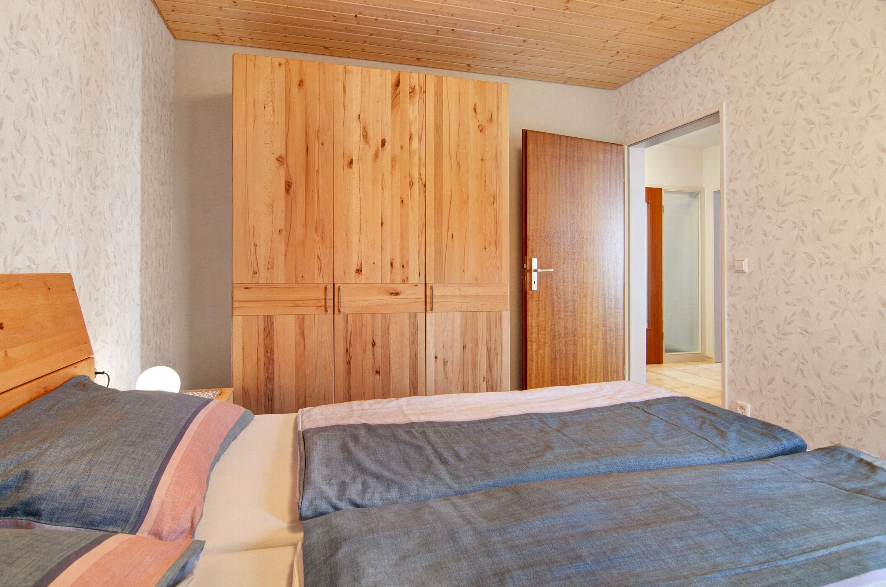 A bedroom with two beds, wooden wardrobe, and a door leading to another room.