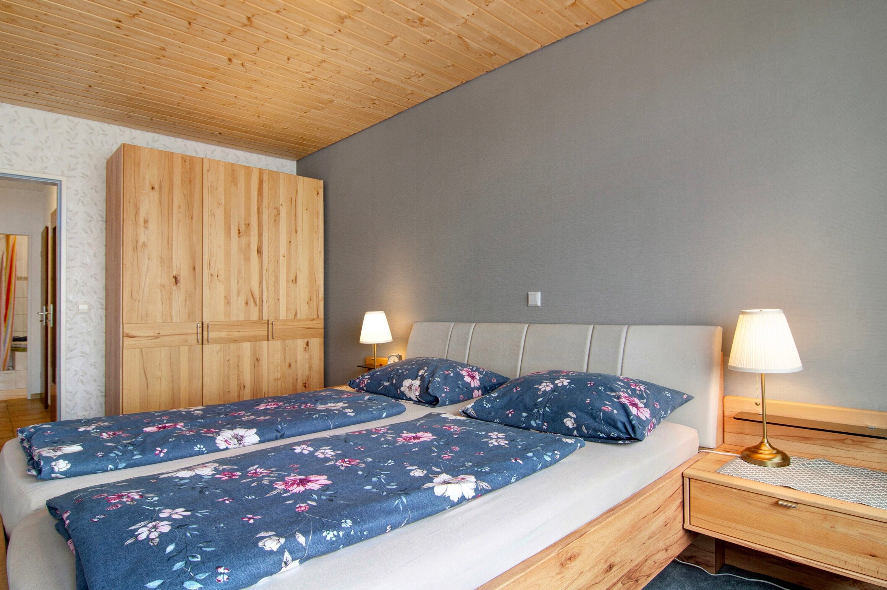 A bedroom with a bed, two bedside tables, a wooden wardrobe, and a lamp.