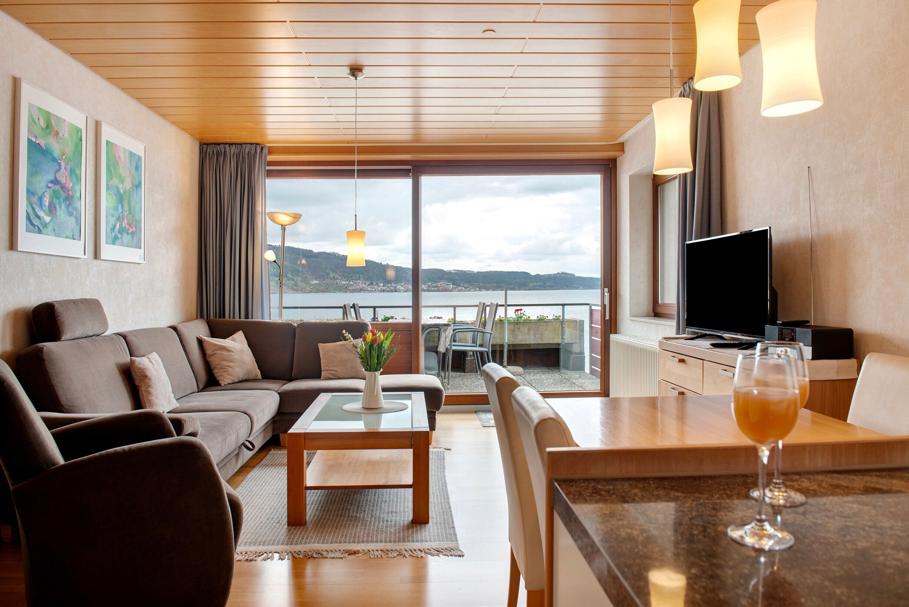 A modern living room with a sofa, coffee table, and dining area, a TV, and a view of a body of water.