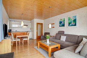A modern living room with a wooden ceiling, a sofa, a coffee table, and a dining area with chairs and a table.