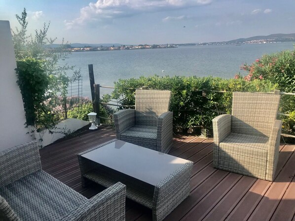Une terrasse dotée de meubles en osier, d’une table en verre et offrant une vue sur la mer.