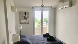 Ein Schlafzimmer mit Bett, einer Kristallleuchter, einem Gemälde und Blick durch eine Tür.