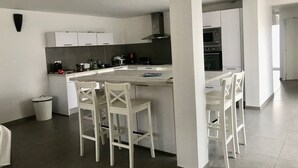 Eine moderne Küche mit weißen Schränken, einer zentralen Kochinsel mit Barhocker und einem sichtbaren Mülleimer.