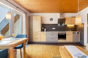 Una cocina moderna con armarios de madera, horno integrado y comedor con mesa y sillas.