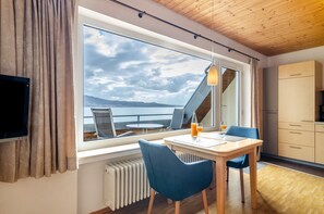 Una habitación con un ventanal grande, una mesa con dos sillas, un televisor y una zona de cocina.