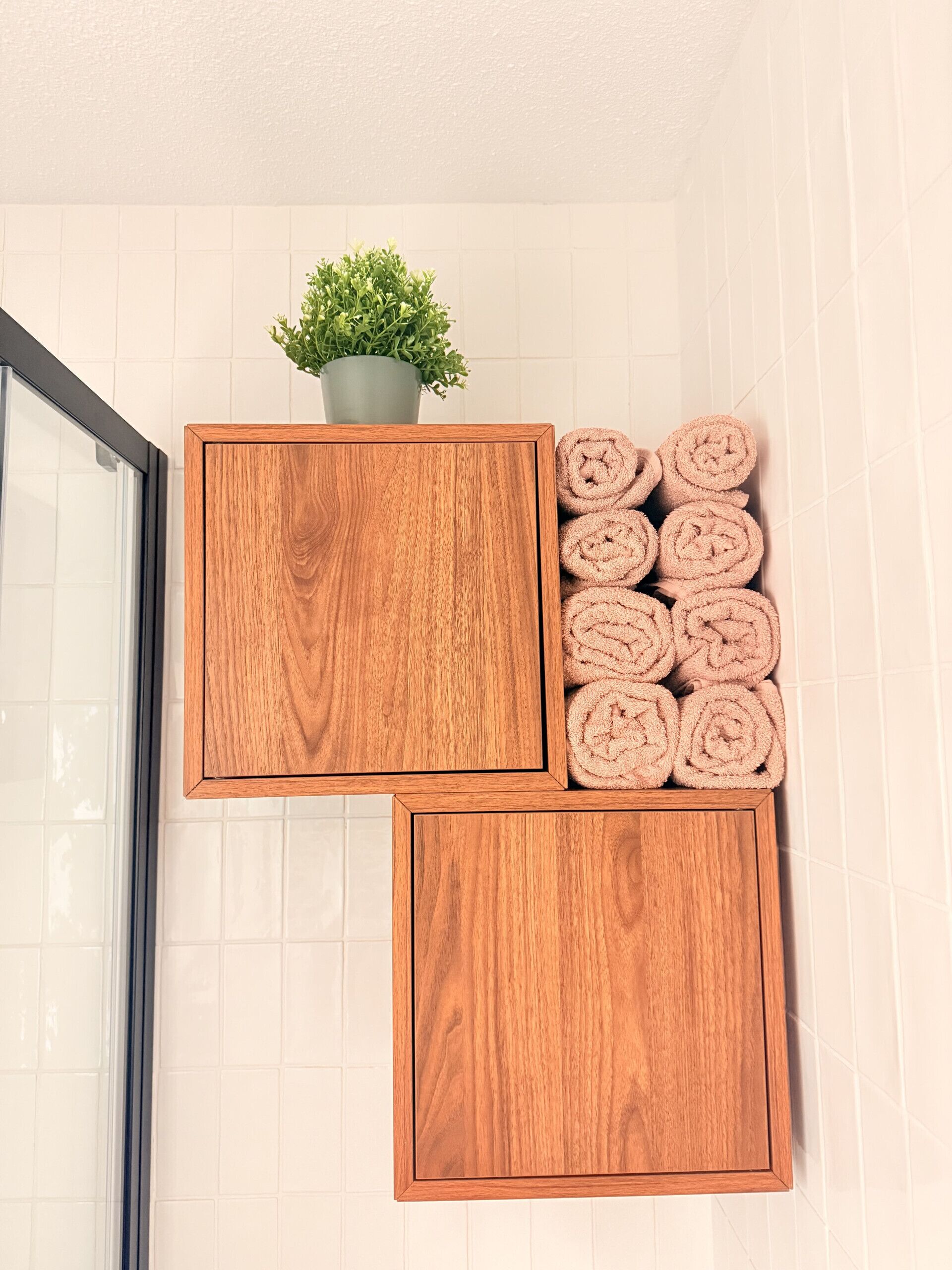 A bathroom with wooden cabinets, a potted plant, and rolled towels.