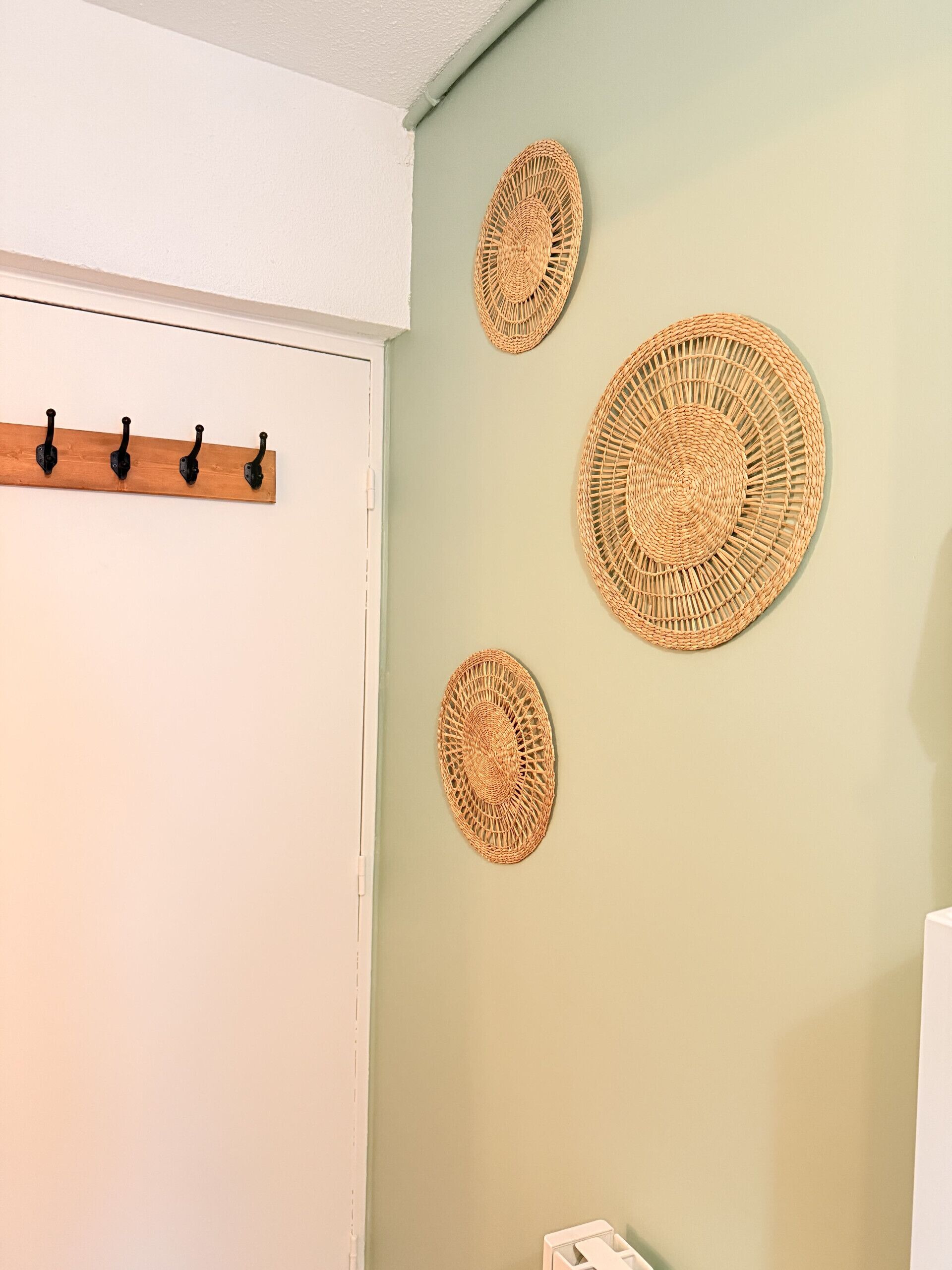Een kamer met een witte deur, een houten kapstok met vier haken, en drie wanddecoraties.