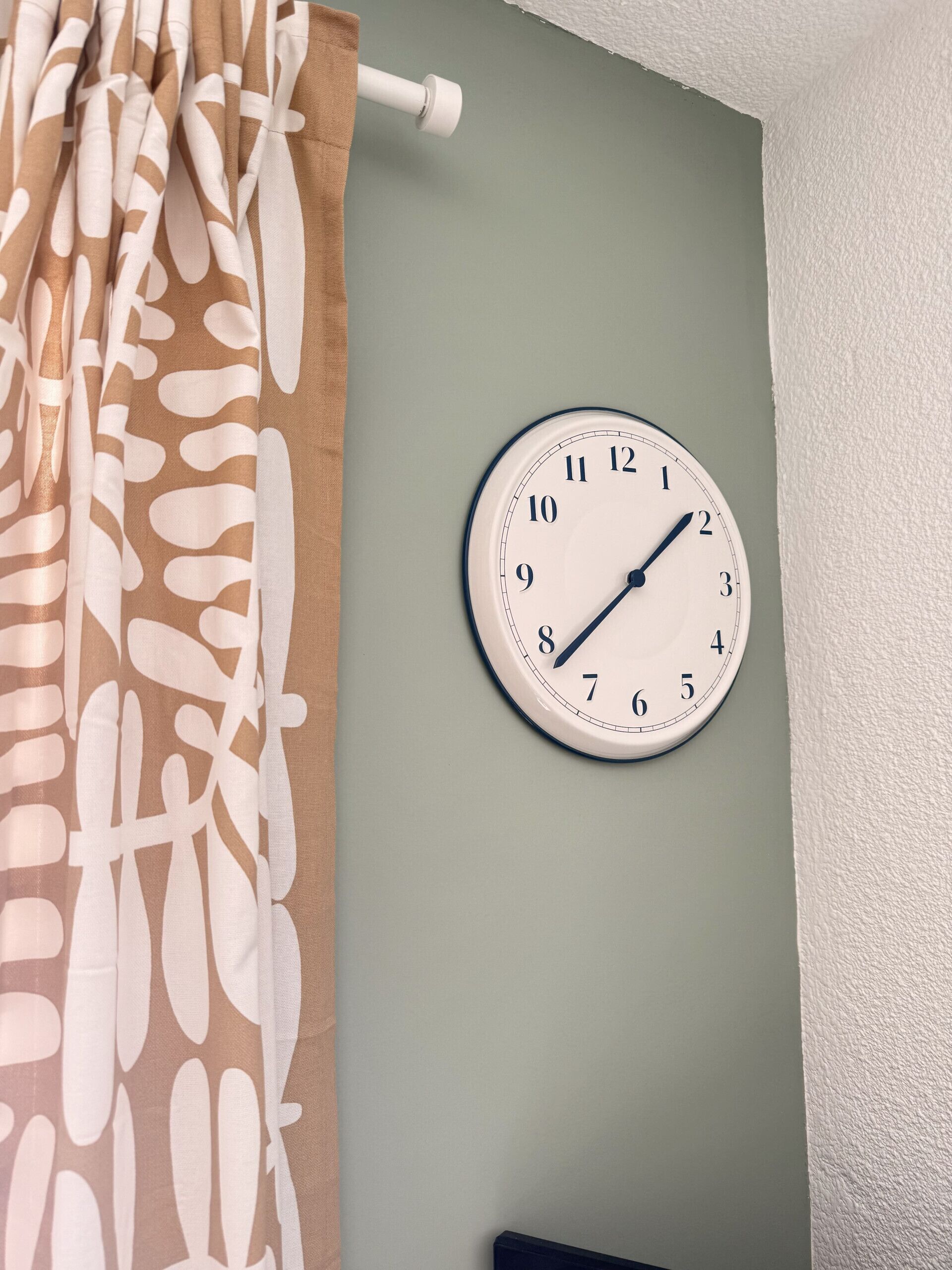 Een wandklok met een eenvoudig ontwerp, bevestigd aan een lichtgroene muur.