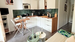 Un espacio habitable compacto con kitchenette, zona de comedor y sala de estar con sofá y una mesita redonda.