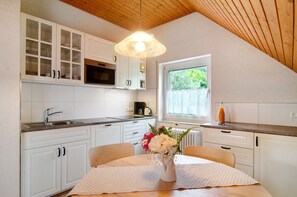 A kitchen with white cabinets, a dining table with a vase of flowers, and a window with a view of greenery.