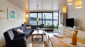 A modern living room with a sofa, coffee table, and dining table, a TV, and a scenic lake view. - Apartment '1, 70sqm' with Large Terrace Right on the Lake (Bodman-Ludwigshafen)