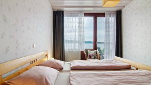 A room with two beds, a window with curtains, a view of the sea, and a wooden ceiling. - Apartment '1, 70sqm' with Large Terrace Right on the Lake (Bodman-Ludwigshafen)