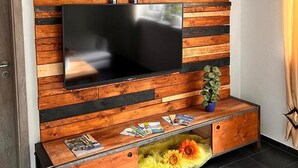 Un mueble moderno de entretenimiento con televisor de pantalla plana, paneles de madera y un estante inferior con revistas y una planta en maceta.