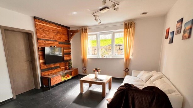 Una sala de estar con un televisor montado en una pared de madera, un sofá, una mesa de centro y una ventana con cortinas.