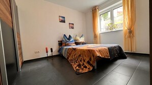 Un dormitorio con una cama, una ventana con cortinas, una pared con un cuadro y una puerta.