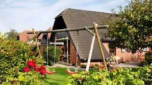 Ein Garten mit Schaukel, einem Ziegelhaus und einer überdachten Terrasse.