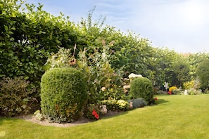 A well-maintained garden with neatly trimmed hedges, a variety of flowering plants, and a clear sky.