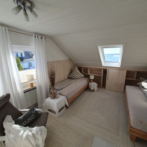 Ett mysigt, litet rum med ett sluttande tak, en säng, ett litet bord, en stol och ett fönster med utsikt över en byggnad.
