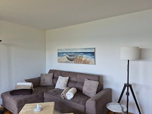 A living room with a brown sofa, a painting of a beach scene, a floor lamp, and a small table with a tissue box.