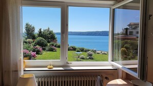 A room with a large window offering a view of a lake and greenery. - Apartment 'Panorama-seetraum' with Lake View, Private Terrace and Wi-Fi (Sipplingen)