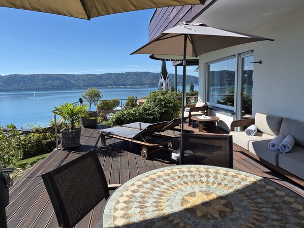 A balcony with a view of a lake, a table with a patterned tablecloth, and a sofa with towels.