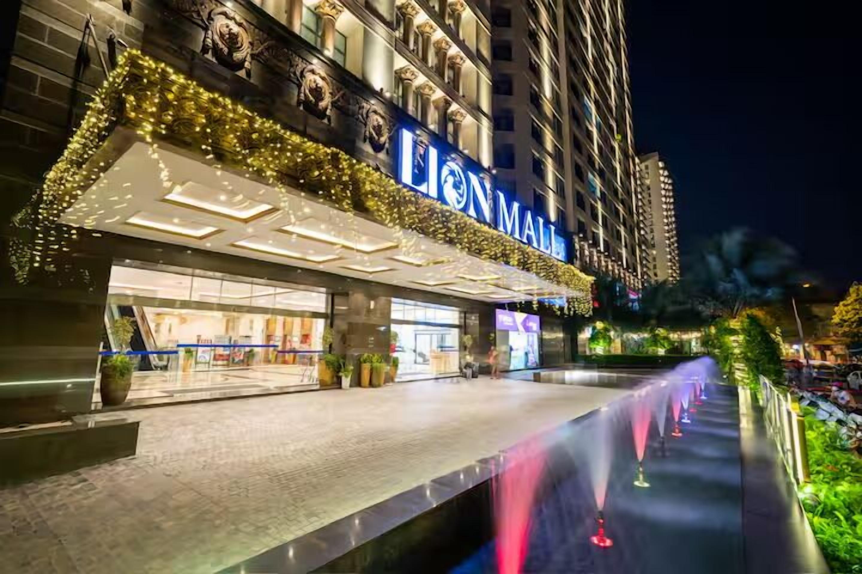 A hotel with a prominent "LION MALL" sign, a well-lit entrance, and a water feature in front.