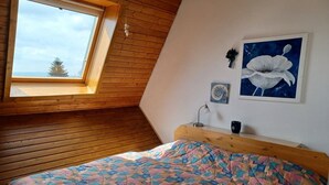 A bedroom with a sloped ceiling, a skylight, a bed with a colorful quilt, a bedside table with a lamp, and two framed artworks on the wall. - Apartment 'Koberstaedt' Panoramic Lake View, Balcony and Wi-Fi (Meersburg)