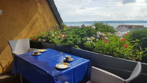 A balcony with a table set for two, covered with a blue tablecloth, and a view of a lake and buildings in the background. - Apartment 'Koberstaedt' Panoramic Lake View, Balcony and Wi-Fi (Meersburg)