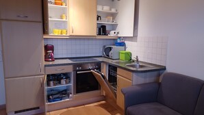 Eine kompakte Küche mit Einbauofen, Mikrowelle und Kaffeemaschine. Es gibt einen Essbereich mit einem Stuhl und einem kleinen Tisch.
