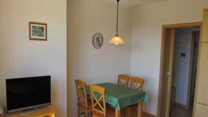 Ein Essbereich mit Tisch, Stühlen, einem Fernseher auf einem Schrank und einer Hängeleuchte.