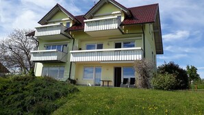 Un edificio de varios pisos con balcones, techo de tejas rojas y un jardín delantero con césped.