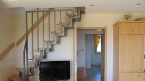 Una escalera de diseño moderno, un televisor en la sala de estar y armarios de madera.