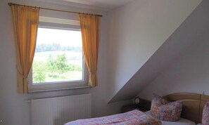 Un dormitorio con ventana, cama, mesita de noche y lámpara.