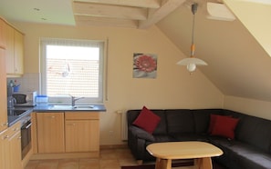 A kitchen with a window, a dining table, and a sofa with red cushions.