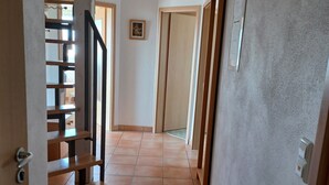 A hallway with tiled flooring, a wooden staircase, and a door at the end.