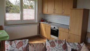 Une cuisine avec des meubles en bois, un pare-feu en carrelage, une fenêtre avec des stores et un canapé agrémenté de coussins à motifs.