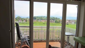 Une pièce dotée d’une porte-fenêtre coulissante donnant sur un balcon extérieur, où se trouvent une chaise et une table.