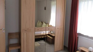 Une chambre avec une armoire en bois, un lit, une petite table et une fenêtre avec des rideaux.