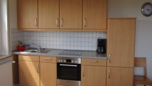 Une cuisine avec des meubles en bois, un four en acier inoxydable, une machine à café et une horloge au mur.