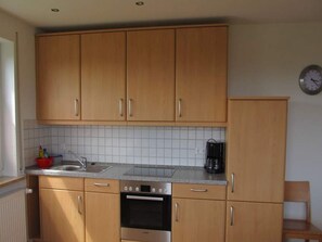 Una cocina con armarios de madera, horno de acero inoxidable, cafetera y un reloj en la pared.