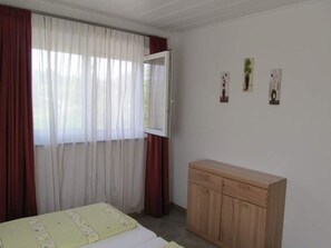 A bedroom with a bed, a wooden cabinet, and a window with sheer curtains.