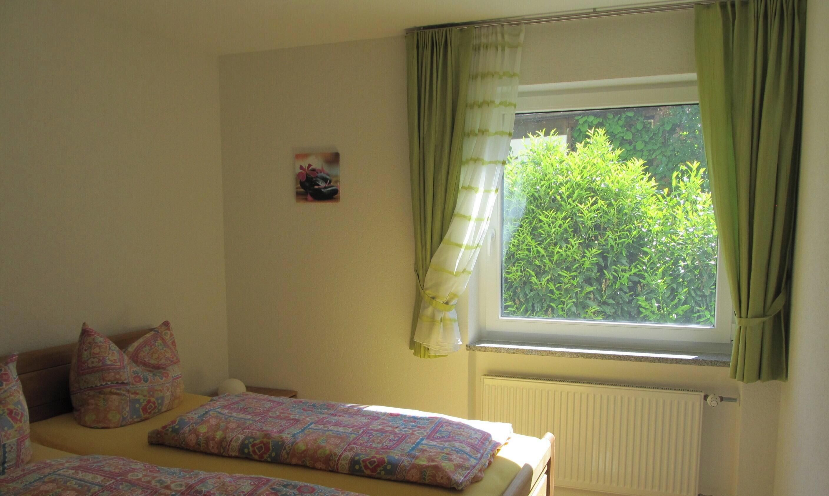 Un dormitorio con dos camas, una ventana con cortinas, un radiador y un cuadro pequeño en la pared.