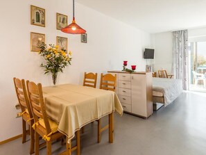 A dining area with a table and chairs, a cabinet, a vase with flowers, and a bed in the background.
