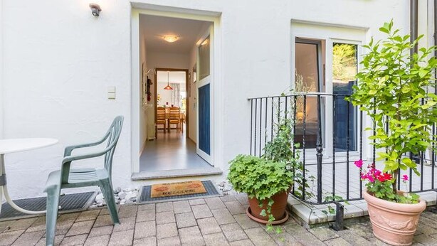 Een binnentuin met een tafel en stoelen, een bloempot en een deur naar een binnenruimte.